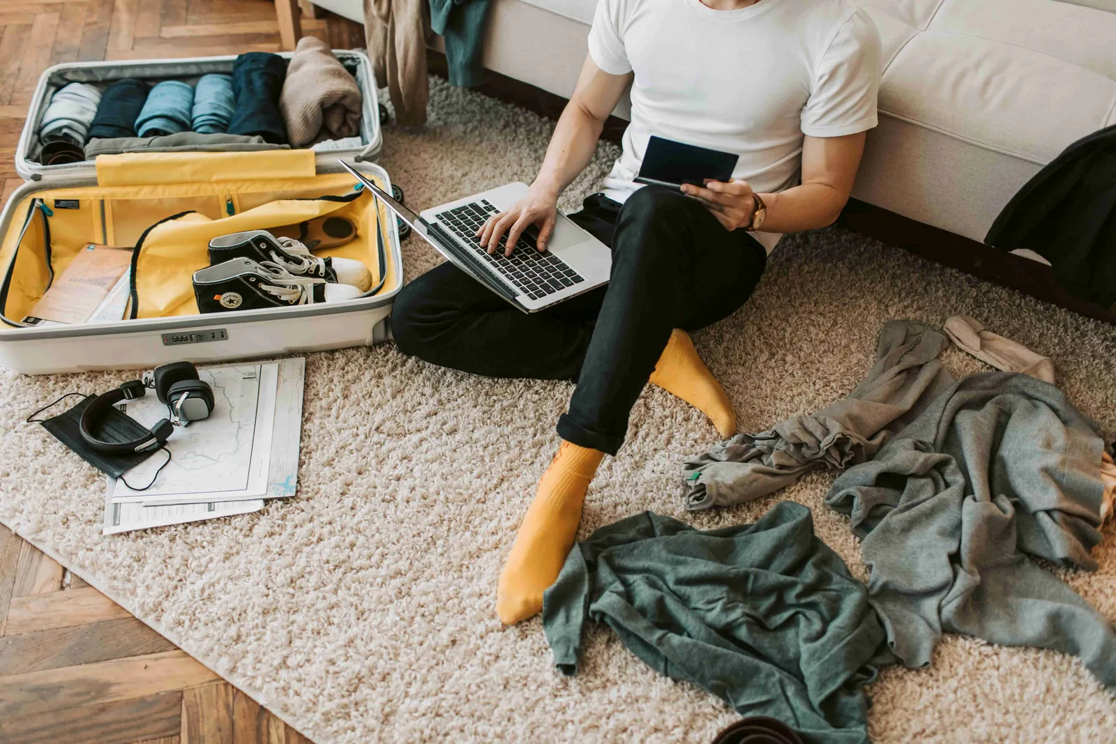 A person packing clothes and shoes into a yellow suitcase on the floor