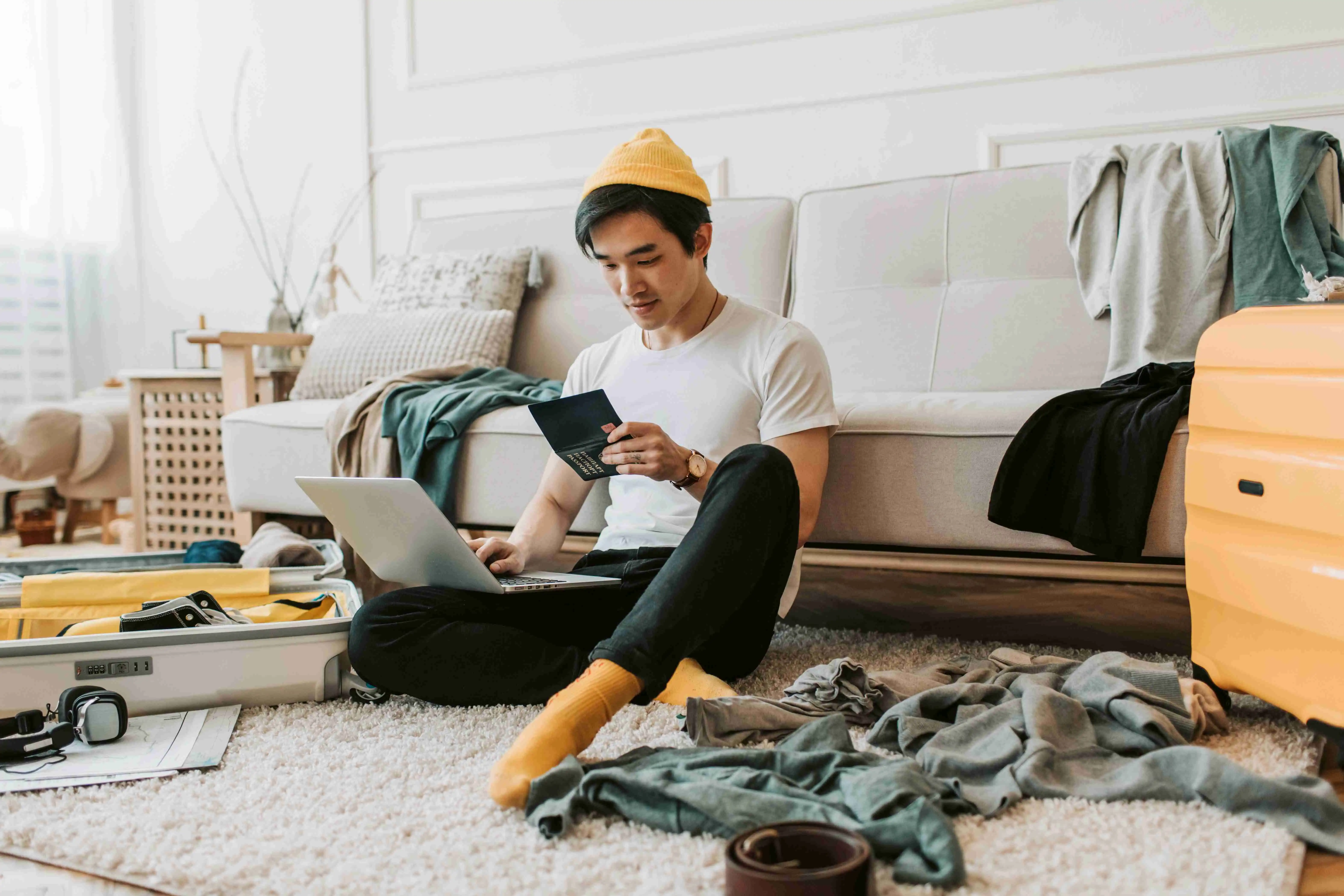 A young man sitting on the floor with a laptop next to a packed suitcase